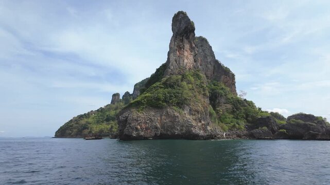 Majestic rock formation rises above tranquil waters, surrounded by lush greenery and a clear sky, creating a picturesque natural landscape ideal for outdoor exploration and adventure photography