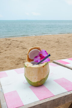 Tropical fresh coconut cocktail decorated with flowers and sandy beach by the sea,tropical resort villa,island summer travel,ocean backdrop,hotel for holiday vacation concept.