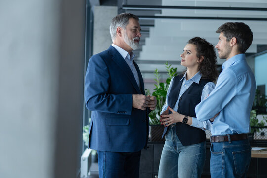 Three busy coworkers discussing project, standing in modern office