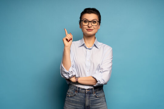 Enthusiastic middle aged woman, entrepreneur points up, eureka gesture, has an idea, on blue background