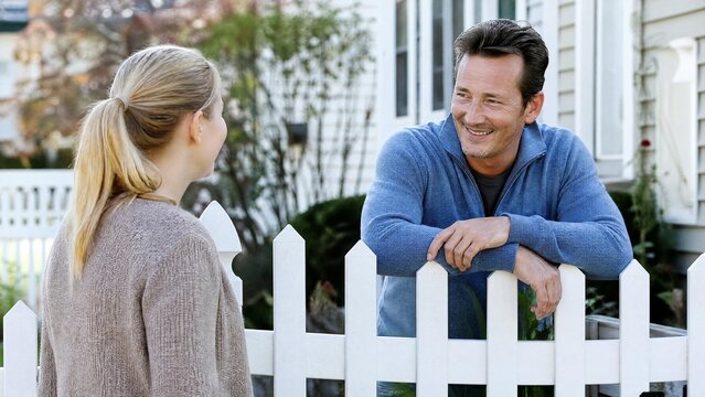 Friendly Neighbors Chatting Over a White Picket Fence in Suburban Yard