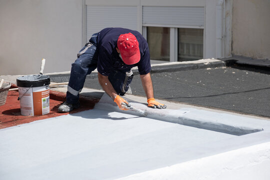 Worker applying a liquid waterproofing membrane with a brush on a rooftop surface