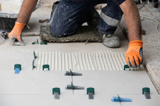 Tiler installing new ceramic floor tiles with adhesive mortar and leveling spacers