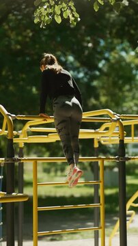 A fit woman performs an intense calisthenics workout on parallel bars at an outdoor gym. Her fitness training takes place in a natural park setting, focused on strength and wellness