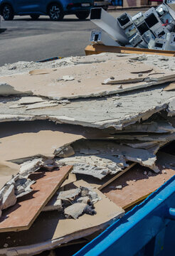 Broken drywall gypsum board and plaster debris piled in construction dumpster with scrap metal at demolition waste site outdoors