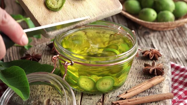 Hand adding sliced unripe green walnuts into a jar with alcohol - preparation of homemade nut liqueur
