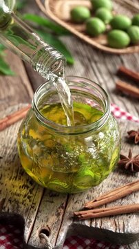 Pouring alcohol into a jar with sliced unripe green walnuts - preparation of homemade nut liqueur or tincture