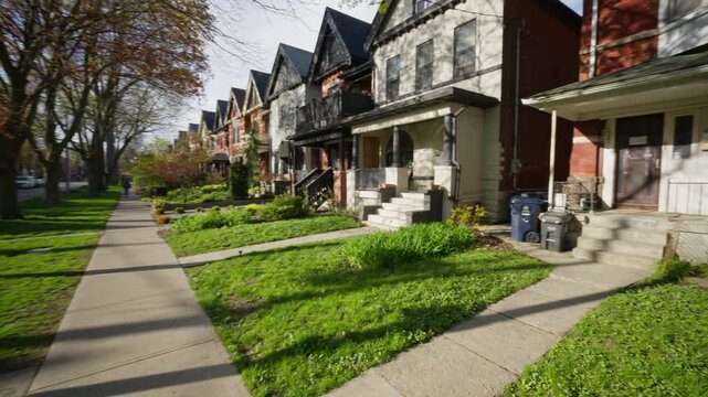 Point of view of a man walking on a sidewalk in spring, entering classic red brick row house on a residential street in an urban neighborhood in North America