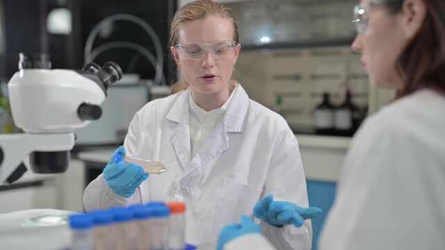 Woman in lab coat discusses microscopic analysis with colleague in science laboratory