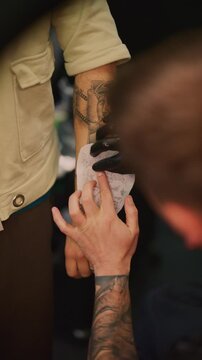 A tattoo artist applies a stencil design to a client's arm. The temporary pattern prepares the skin for the artwork