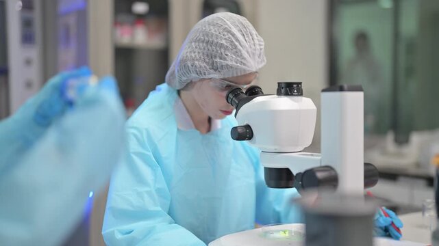 Scientist in protective gear meticulously examines specimen under a microscope in a lab