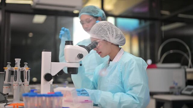 Scientists in laboratory coats and hairnets working with microscopes and test tubes
