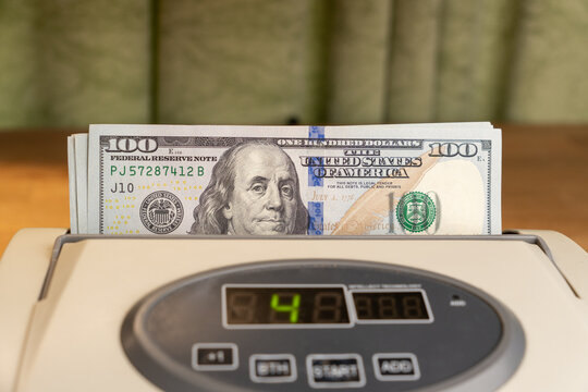 Close up of an automatic banknote counter machine loaded with a stack of 100 dollar bills. Concept of banking, financial operations, wealth, global business, and currency exchange.