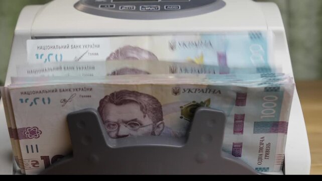 Close up of an automatic cash counter machine fast counting a stack of 1000 Ukrainian hryvnia paper bills. Financial concept of banking operations, cash management, national currency, or economy in
