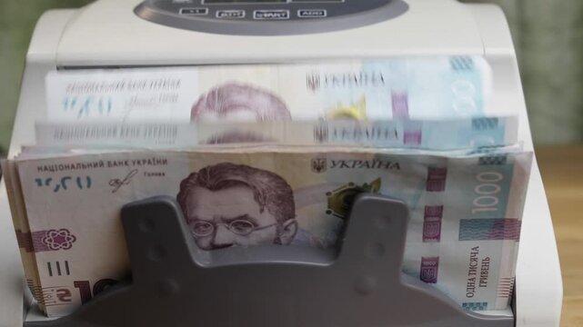 Slow motion close up shot of an automatic banknote counter machine processing a stack of 1000 Ukrainian hryvnia paper bills. Cinematic financial concept of national currency, cash flow, banking, and