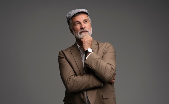 Attractive serious grey-haired man in suit and flat cap isolated on grey