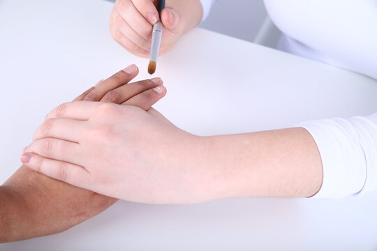  Close-up of a nail technician using a professional brush to apply acrylic gel on a client's fingernail.