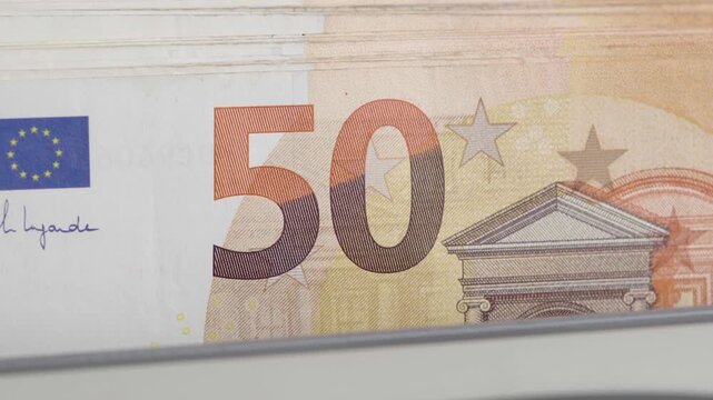 Slow motion close up shot of an automatic banknote counter machine fast processing a stack of fifty euro paper bills. Cinematic financial concept of cash flow, banking operations, currency details