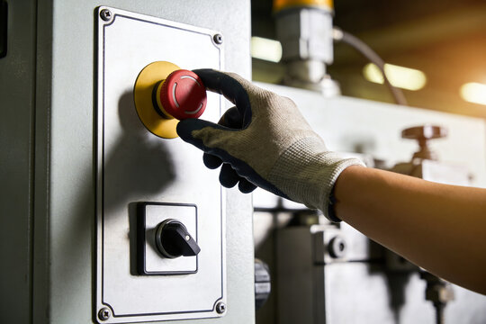 Worker's gloved hand presses red emergency stop button on industrial machinery