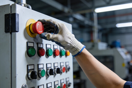 Worker presses emergency stop button on industrial control panel in factory setting