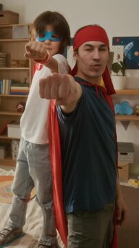Vertical portrait of young adult man and child boy wearing superhero capes, standing back-to-back and punching towards camera. Clip is ideal for Fathers Day and family bonding ads, vertical
