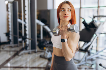 Fototapeta premium Focused woman training with dumbbell in a gym, building strength and maintaining a healthy fitness lifestyle