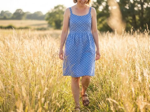 A wonan walks with bare legs in a summer dress next to tall grass