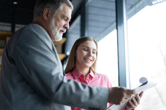 Mature businessman and young business woman professional corporate executive leaders discussing strategy documents