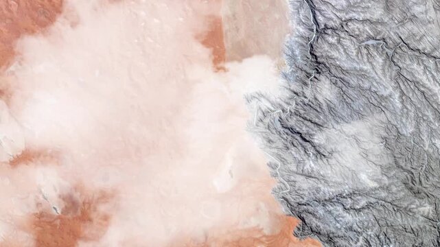 Flying over dramatic desert and rocky terrain boundary with passing clouds satellite view from space