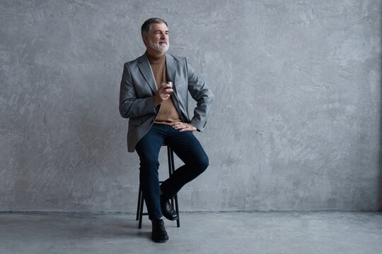 Confident mature businessman chilling relaxing drinking enjoying whiskey against grey wall.