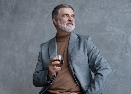 Confident mature businessman chilling relaxing drinking enjoying whiskey against grey wall.