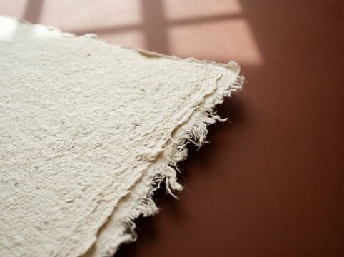 Macro Shot of Handmade Cotton Paper with Fibrous Deckled Edge on Smooth Dark Terracotta Surface with Window Shadows
