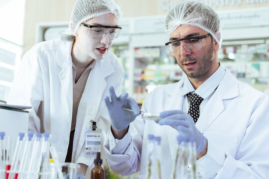 Professional male and female scientists in lab coats and PPE examining samples in petri dish, conducting medical research and clinical experiments in modern laboratory for biotechnology development