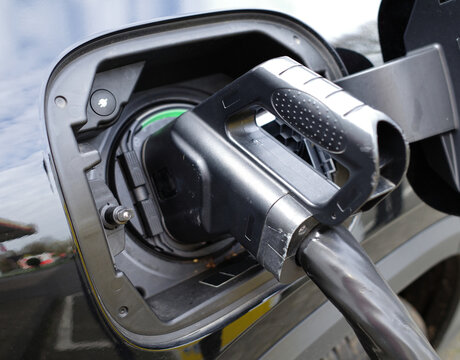 A Combined Charging System (CCS) plug is shown connected to an electric vehicle. The CCS plug is black with a textured grip handle for easy handling. It connects to a charging port on a vehicle