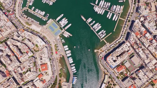 Stunning top-down aerial shot flying over marina zeas, a beautiful harbor in piraeus, greece, filled with numerous luxury yachts and boats docked at the piers on a sunny day