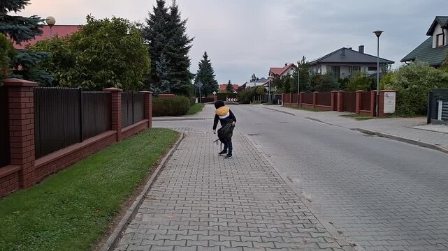 Boy 7 year old walking down quiet street with homes and trees in the evening light in a residential area near a curve in the road