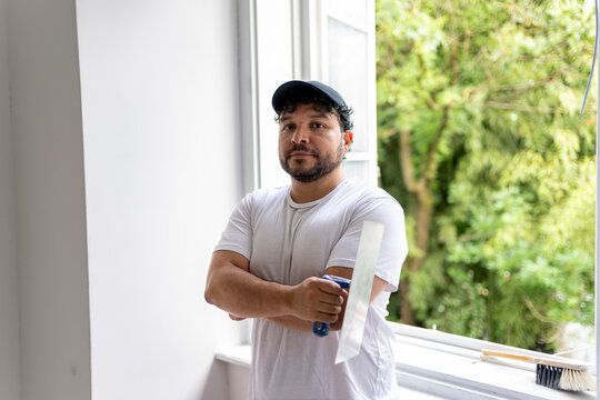 Skilled construction worker holding a plastering trowel near an open window, portrait of professional craftsman during residential renovation work