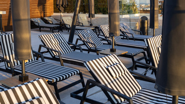 Striped Lounge Chairs and Closed Umbrellas on a Hotel Rooftop Pool Deck at Sunset