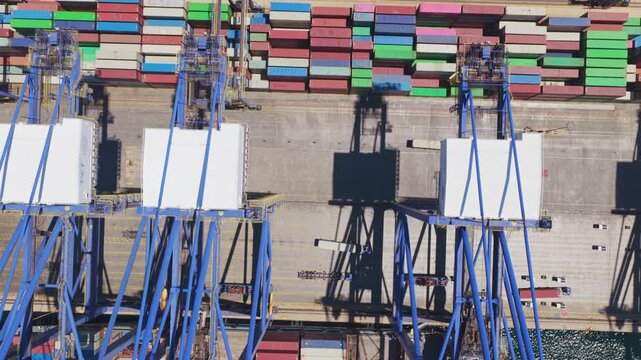 Stunning aerial top-down view of gantry cranes loading and unloading a container ship at a busy industrial harbor, revealing thousands of colorful stacked containers at the commercial port