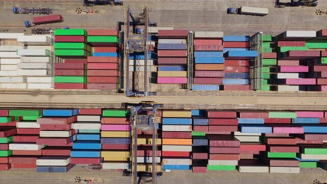 Aerial top-down view showing a gantry crane organizing colorful cargo containers at a busy port terminal, illustrating the complexity of global logistics and international shipping