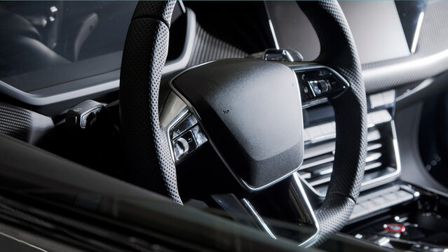 Close-up of a modern car steering wheel with dashboard controls and interior details visible in a luxury car setting.