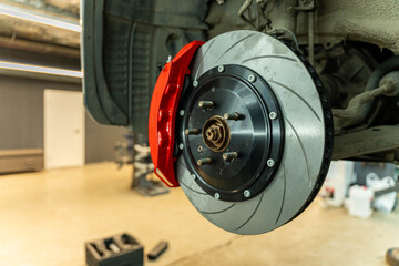Close-up view of a vehicle wheel brake assembly with a ventilated disc and red caliper mounted in an auto repair workshop, with the car raised and tools © Egor Lint
