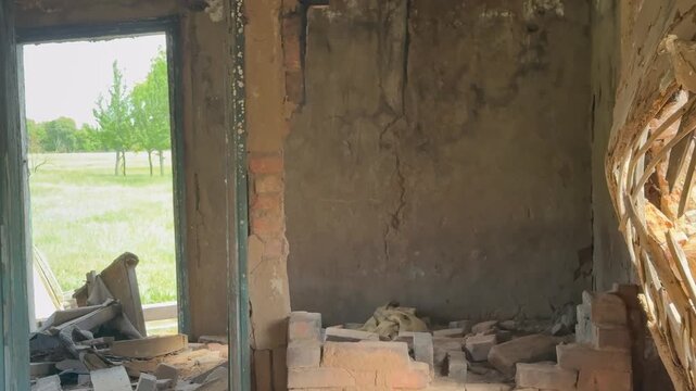 a dilapidated room with cracked walls and debris scattered on the floor. Outside the window, a green field is visible, adding contrast to the room's decay.