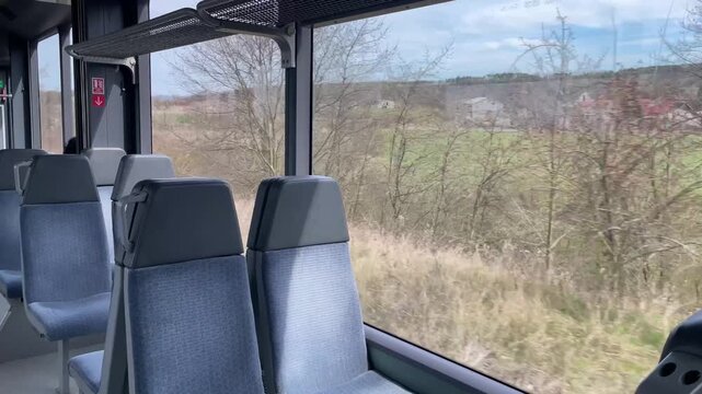Empty bus seats by window showing passing countryside and leafless trees, modern gray fabric seats, quiet overcast day, gentle motion of coach along rural