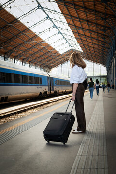 Elegant mid-adult woman walking on a train station platform pulling a suitcase, business travel concept.