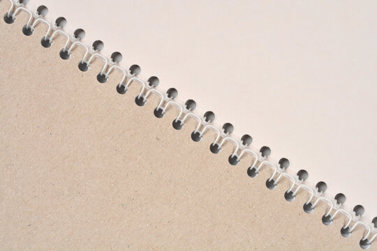 A detailed diagonal view of a white plastic spiral comb binding connecting a brown kraft paper cover to blank pages