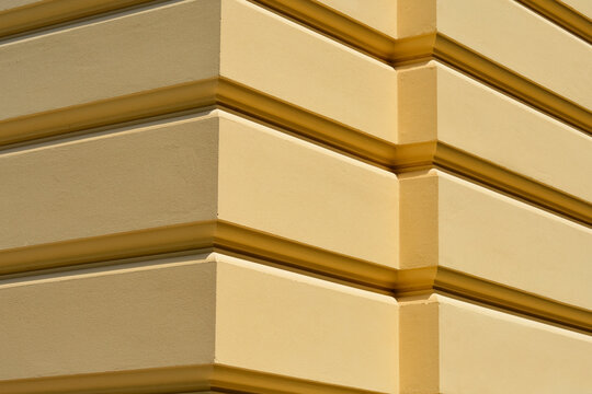 An architectural close up of a yellow painted building facade corner featuring classic horizontal rusticated groove patterns