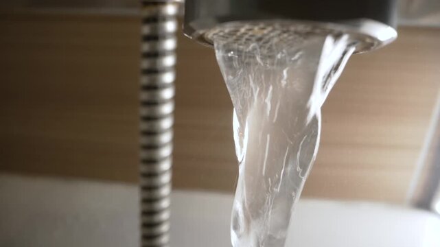 A closeup shot captures clear water pouring from a modern kitchen faucet aerator into a sink, with a flexible metal hose visible in the background