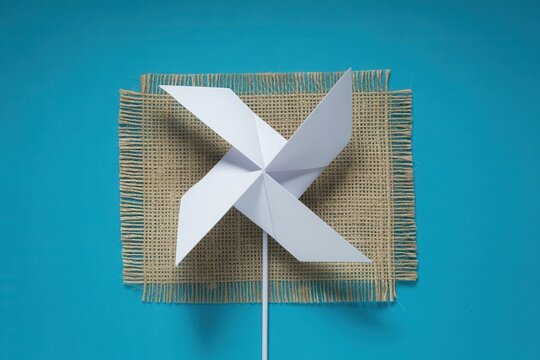 A white paper windmill on a burlap mat against a blue background