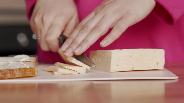 The housewife cuts the cheese with a knife in order to add it to the sandwich filling.